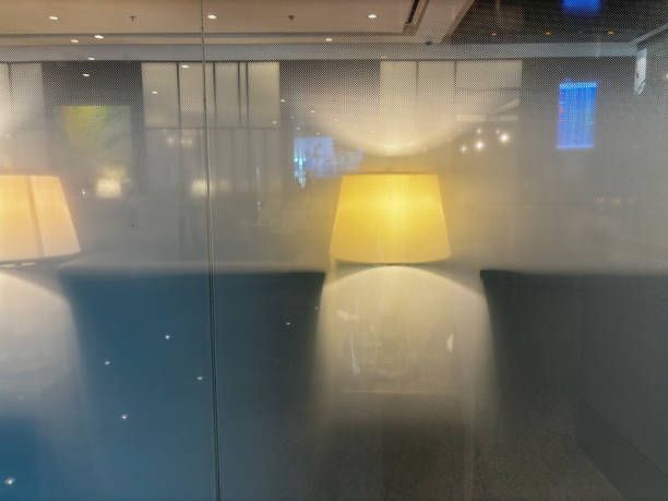 Two lamps with a white shade, one of which is lit. The lamps are placed in front of a window, and the light from the lamps is reflected on the window. The scene has a warm and cozy atmosphere