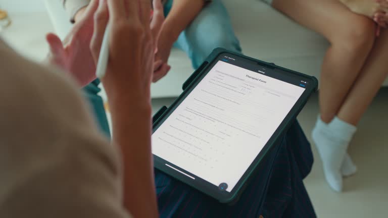 Asian sadness couple doing a mental health survey on a tablet with a female psychotherapist. Professional social worker assist married couples with empathy.