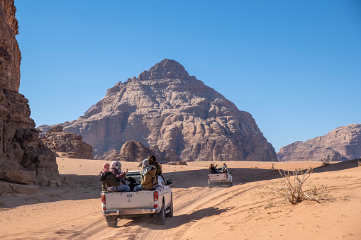 Excursion group of tourists rides on pickup truck through Wadi Rum desert which is UNESCO World heritage site in Jordan, Middle East.
