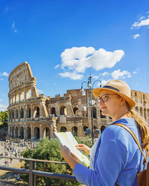 Photo of Happy woman tourist looking up from map at Rome Colosseum. Travel guide in Rome.