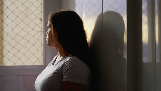 istock Contemplative Young Female Leaning Against Wall, Peering Out Window, Sensing Loneliness. Deeply Reflective Woman in 20s Alone in Room 2086586914