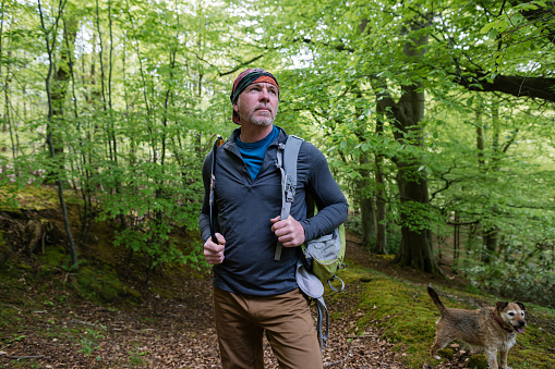 A medium close up of a mature man who is stopping for a moment to feel grounded whilst on an outdoor hike in Northumberland in the North East of England. He is wearing a rucksack and a bandana on his head. He is enjoying some time on his own with his dog.