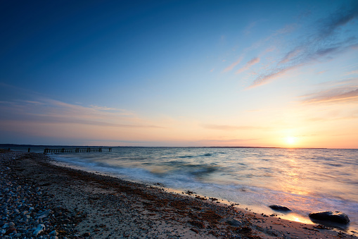 Scenic view of beach with coastline and abandoned pier over sea against orange tranquil sky during sunset