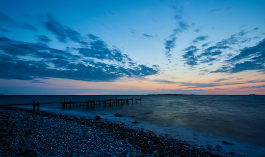 Abandoned pier over sea and beach at coastline against idyllic blue cloudy sky with horizon at sunset