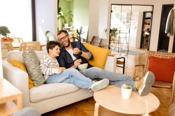 istock Playful father and son sharing food while watching TV 2086641826