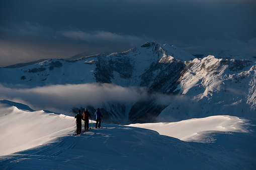 Three male skiers stand on a snowy slope and admire a mountain massif, part of which is covered by a small band of fog