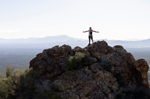 Mature man stretches arms out on rock ridge above valley and mountains, Tucson Mountain Park, Arizona