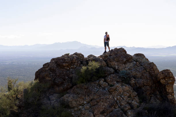 Mature man stands on rock ridge crest above valley and mountains, Tucson Mountain Park, Arizona