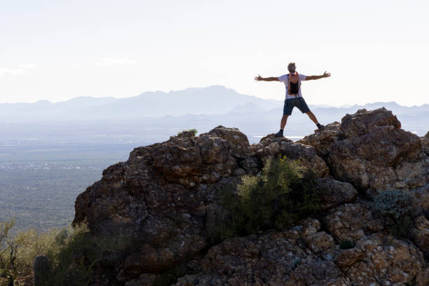 Mature man stretches arms out on rock ridge above valley and mountains, Tucson Mountain Park, Arizona