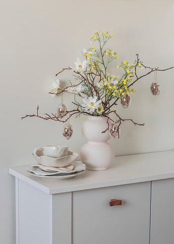 Ceramic white tableware, Easter decor, Easter bouquet on a white wooden buffet in the living room. Holiday mood concept