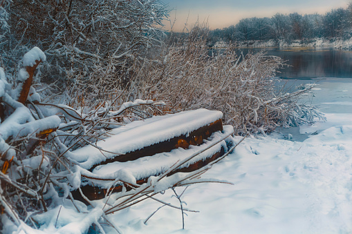 overturned boat on the river bank in winter under snow