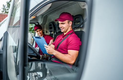 Cheerful male and female courier in delivery van, ready to deliver