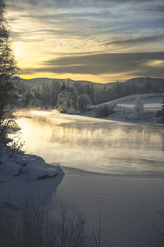 A scenic morning landscape with snowy river, fog, and trees
