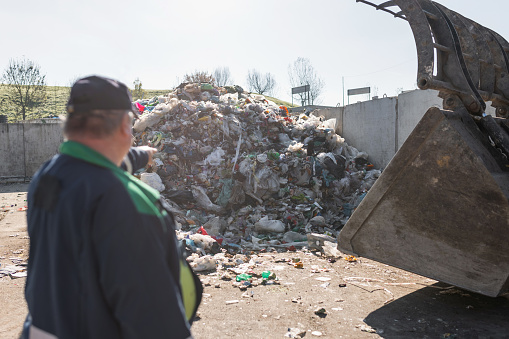 Landfill worker directing skid steer loader on the garbage heap. Waste disposal, consolidation, and transfer concept.