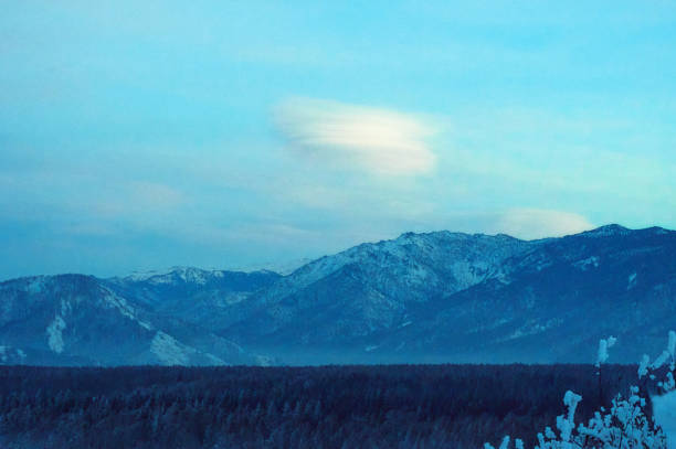Cold snowy mountain landscape at sunset. Lenticular clouds. Panoramic view of snowy mountain peaks and slopes of North Chuyskiy ridge at sunset. Russia, Siberia, Altai mountains.