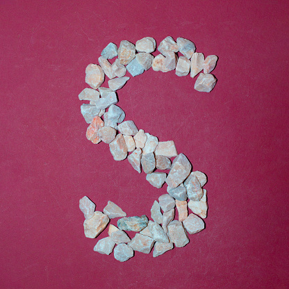 Letter S made of white stones. Creative alphabet concept on a red background.