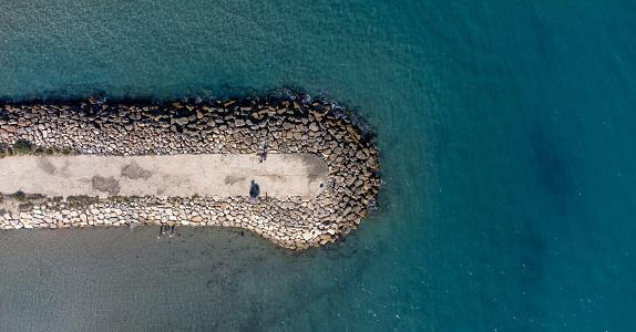 Top view of a breakwater with large boulders jutting into the sea. Surrounded by a calm sea. Ideal for backgrounds or travel concepts. Space for text