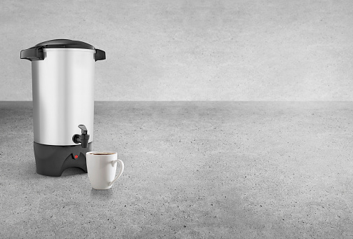 Hot water and coffee dispenser with a coffee mug on an industrial cement surface
