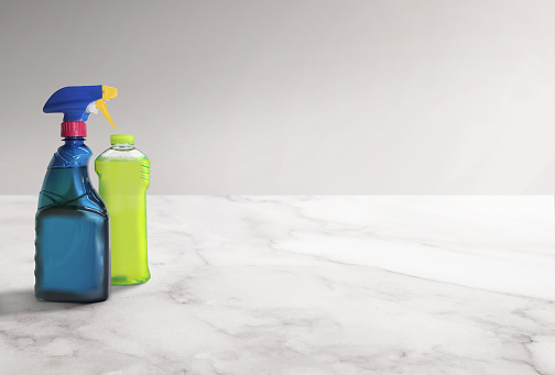 Cleaning products in a spray bottle and a plastic bottle on a white marble