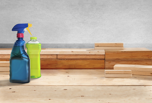 Cleaning products in a spray bottle and a plastic bottle on a wood surface
