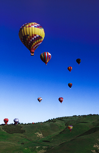 Distant vertical image of hot air balloons ascending into a cloudless sky over Laguna Raceway.\n\nTaken in Laguna Seca, California, USA.
