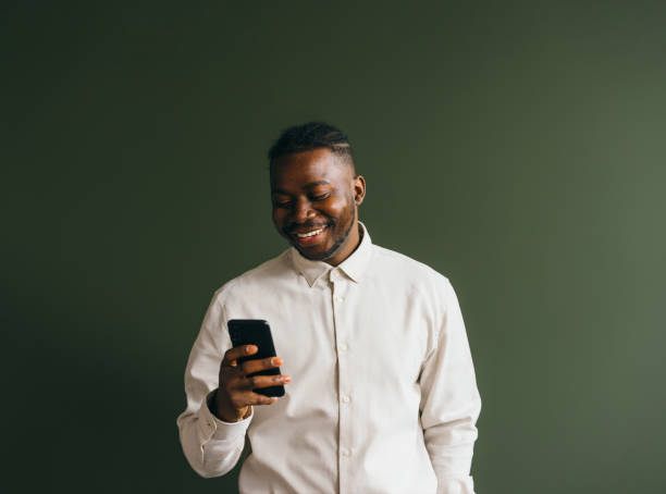 Smiling Man in White Shirt Using Smartphone on Green Background