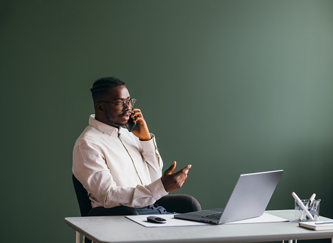 Focused businessman talking on phone using laptop in home office