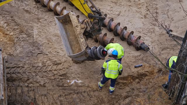 Construction Company Worker Preparing Long Industrial Drill For Pile Driver Machine
