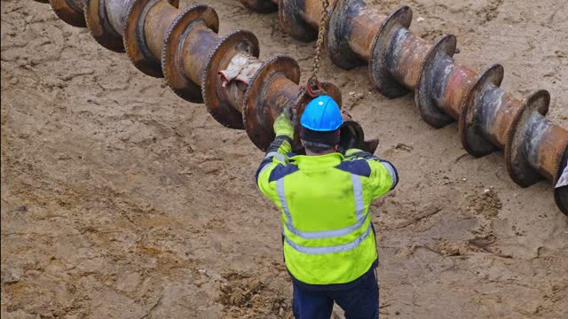 Construction Company Worker Preparing Long Industrial Drill For Pile Driver Machine