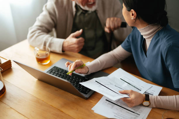 istock Unrecognizable Nurse Holding Bills And Pen While Using A Laptop Computer And Talking With A Senior Man 2087258766