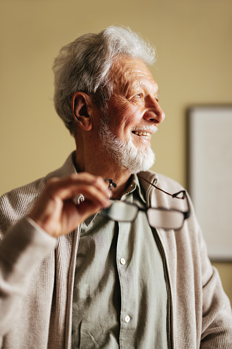 Low angle view of a happy old man holding his eyeglasses and looking away.