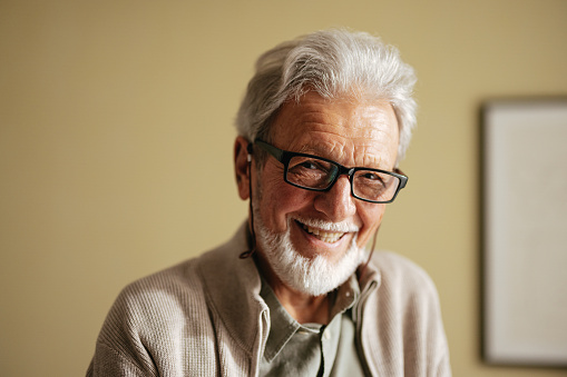 Close up photo of a smiling old man with eyeglasses looking at camera.