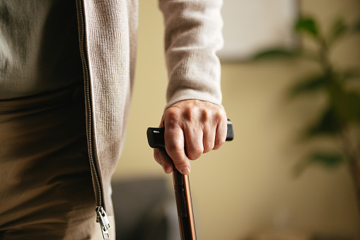 An anonymous old man walks with a walking cane at the nursing home.