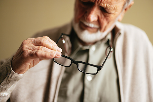 Unrecognizable worried old man sitting at the nursing home, focus on his hand and eyeglasses.