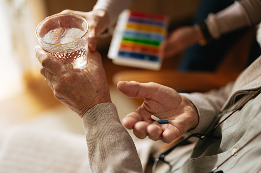 Close up of an unrecognizable senior man holding a glass of water and some pills in his other hand, ready to take his daily medicine.