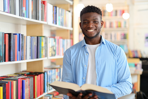 A studious young man in a library, surrounded by books, embodies the pursuit of knowledge and education.