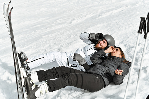 Skiing Couple Looking Through Hand Imitated Scope While Lying Down On Mountain
