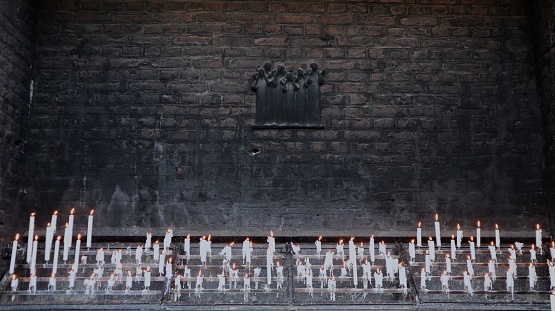 Thin white candles on the soot-blackened exterior wall of a church provide spiritual, warm light at a Catholic pilgrimage site in Germany