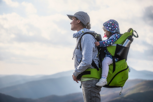 Mom with baby in hiking carrier on a mountain hike at sunset. Hiking weekend.