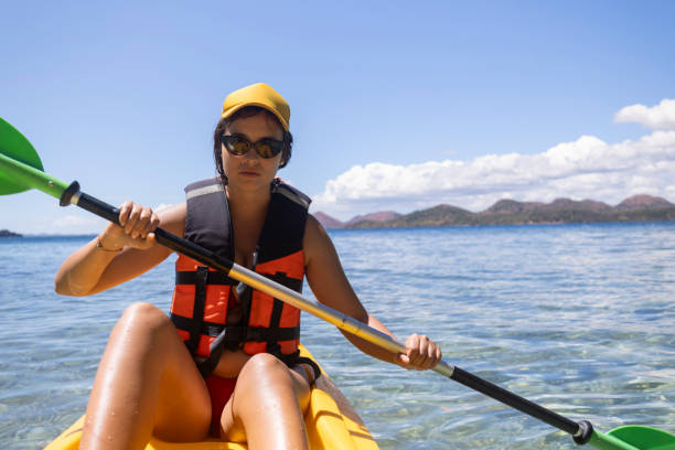 женщина в спасательном жилете и шляпе гребет на байдарке по морю - women kayaking life jacket kayak стоковые фото и изображения