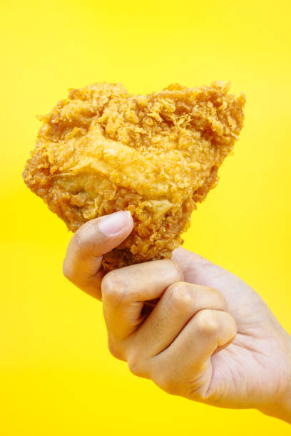 istock Female hand holding fried chicken on yellow background. 2087371780
