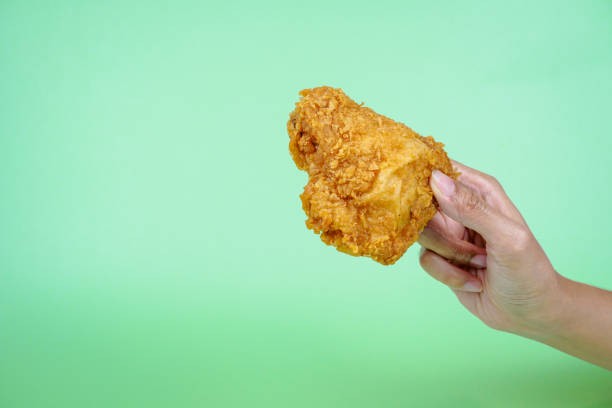 istock Female hand holding fried chicken on green background. 2087383098