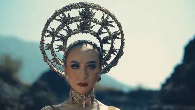Woman in avant-garde headpiece and makeup posing in a dramatic outdoor setting.