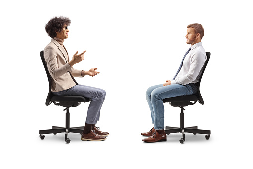 Profile shot of two men sitting in office chairs and talking isolated on white background