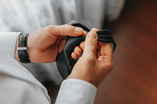 man's tie in hands, close-up photo of hands. The groom is preparing for the ceremony