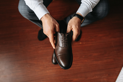 a man in a white shirt, laces up brown shoes and prepares to meet his bride. The man wears classic brown shoes