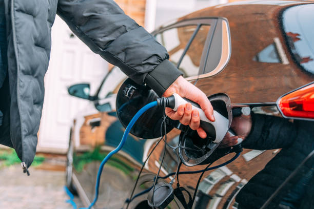 istock Young Man Wearing a Jacket Attaching Charging Cable a Black Electric Car At Home 2087534232