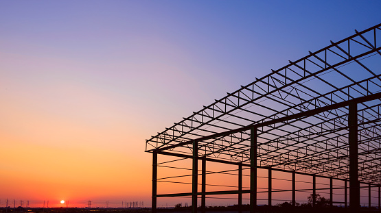 Silhouette metal warehouse building outline structure in construction site against beautiful sunset sky background in industrial settlement zone