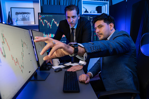 Stock exchange traders looking on high profit chart investment on screen monitor at night time. Businessman partners discussing exchange trading technology growth in neon light at workplace. Sellable.