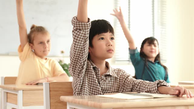 Smart boy raising hand for asking and answering teacher at classroom. Pedagogy.